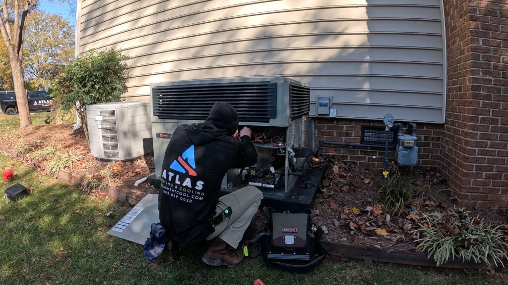 Atlas Heating and Cooling technician in branded jacket working on an outdoor AC system